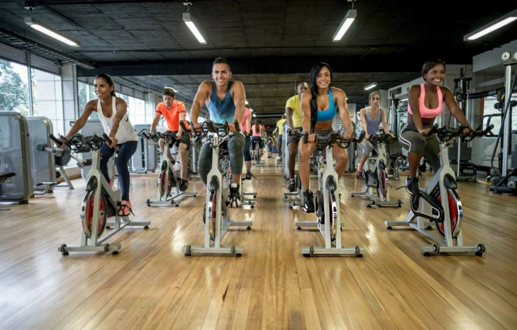 Instructora guiando una sesión de spinning con música y micrófono en un salón deportivo.