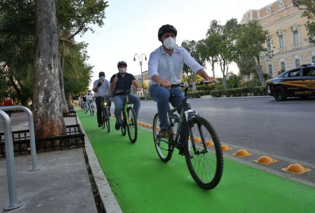 Grupo de ciclistas transitando por una vía verde protegida con delimitadores, frente a edificios históricos del Paseo de Montejo. Parte de la red de ciclovías en Mérida