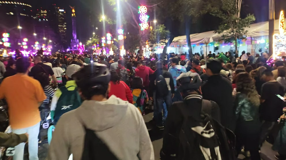 Ciclistas y peatones participando en el recorrido nocturno del Día de Muertos en la CDMX, rodeados de luces festivas, disfraces y decoraciones alusivas a la tradición mexicana.